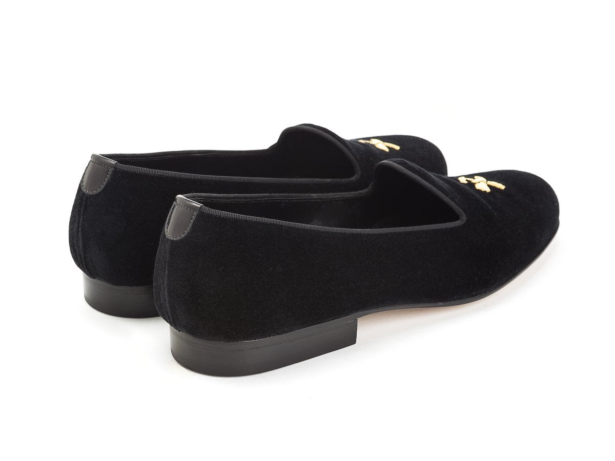 Back angle view of Edward Green Albert slippers in black velvet with hand embroidered gold Double Monk logo on toe