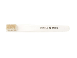 Top view of toothbrush sized bone shoe polishing brush with natural bristles showing Double Monk logo