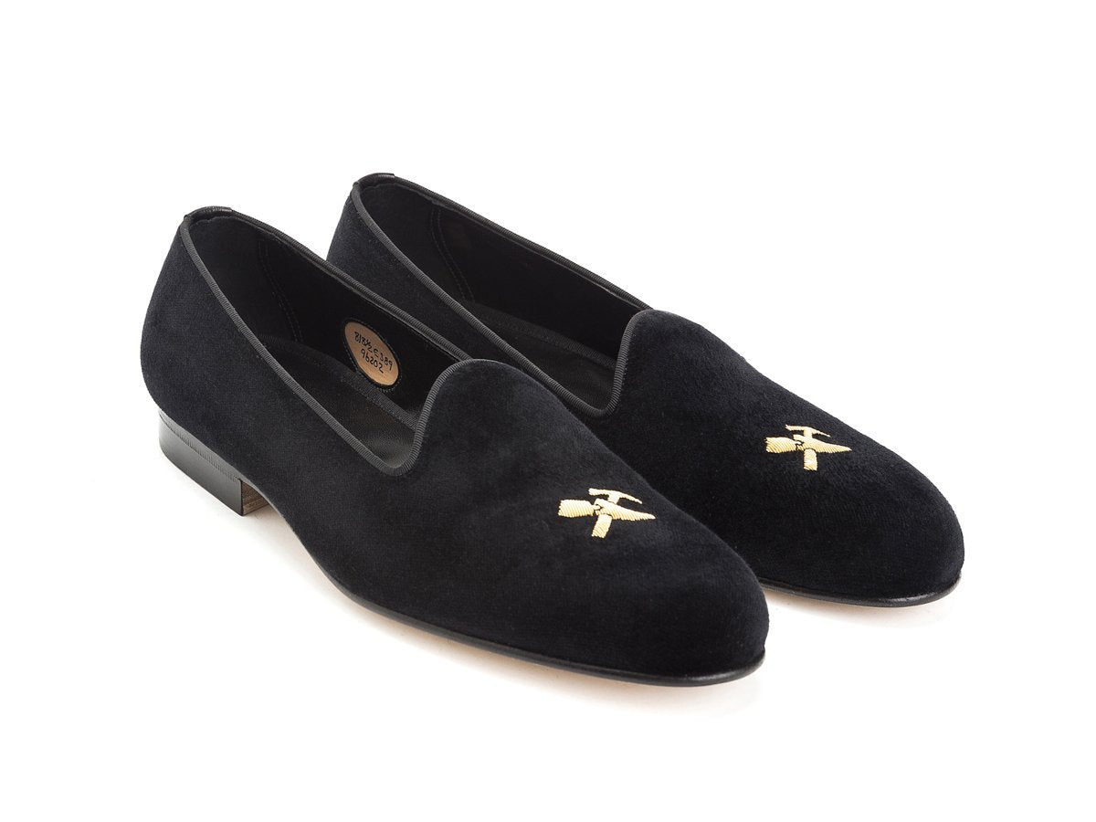 Front angle view of Edward Green Albert slippers in black velvet with hand embroidered gold Double Monk logo on toe