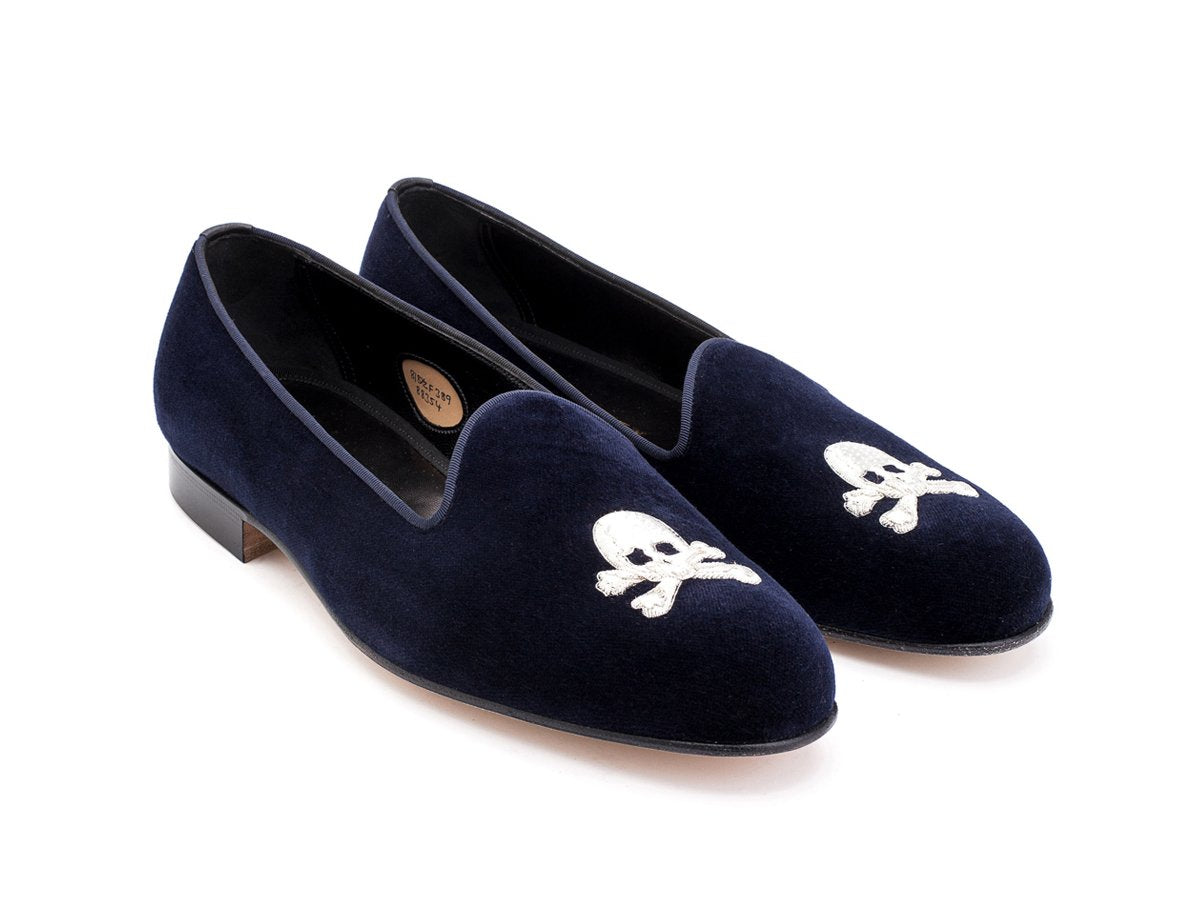 Front angle view of F width Edward Green Albert slippers in navy velvet with hand embroidered silver skull and crossbones motif on toe
